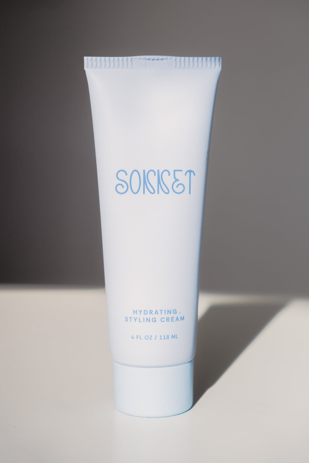 A light blue squeeze tube of SONNET Hydrating Styling Cream standing upright on a white surface against a dark gray background.