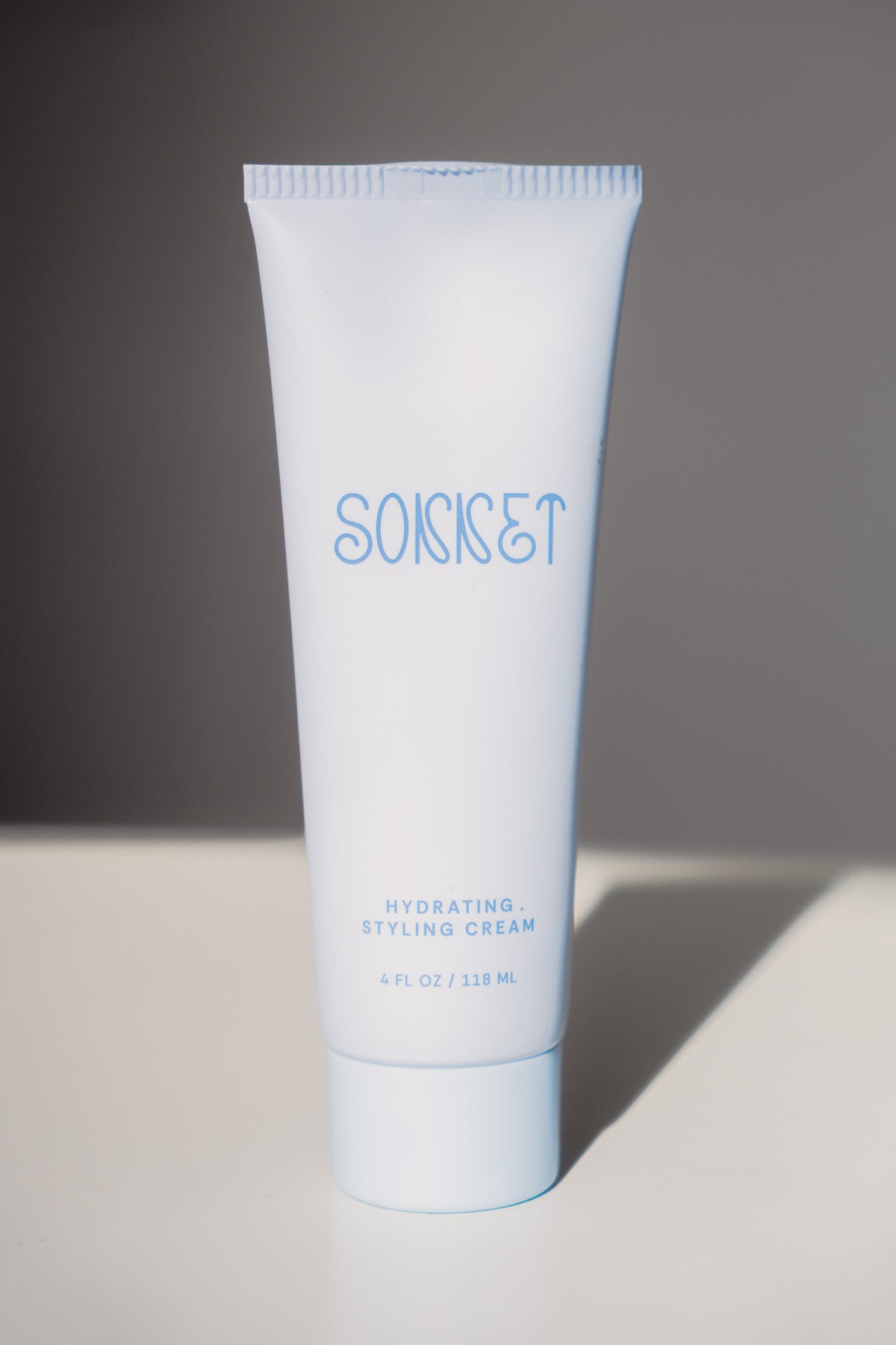 A light blue squeeze tube of SONNET Hydrating Styling Cream standing upright on a white surface against a dark gray background.