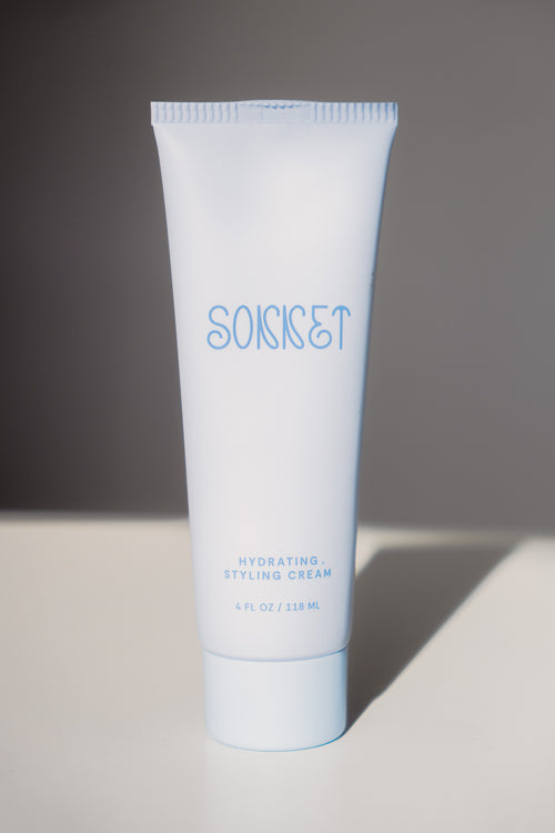 A light blue squeeze tube of SONNET Hydrating Styling Cream standing upright on a white surface against a dark gray background.
